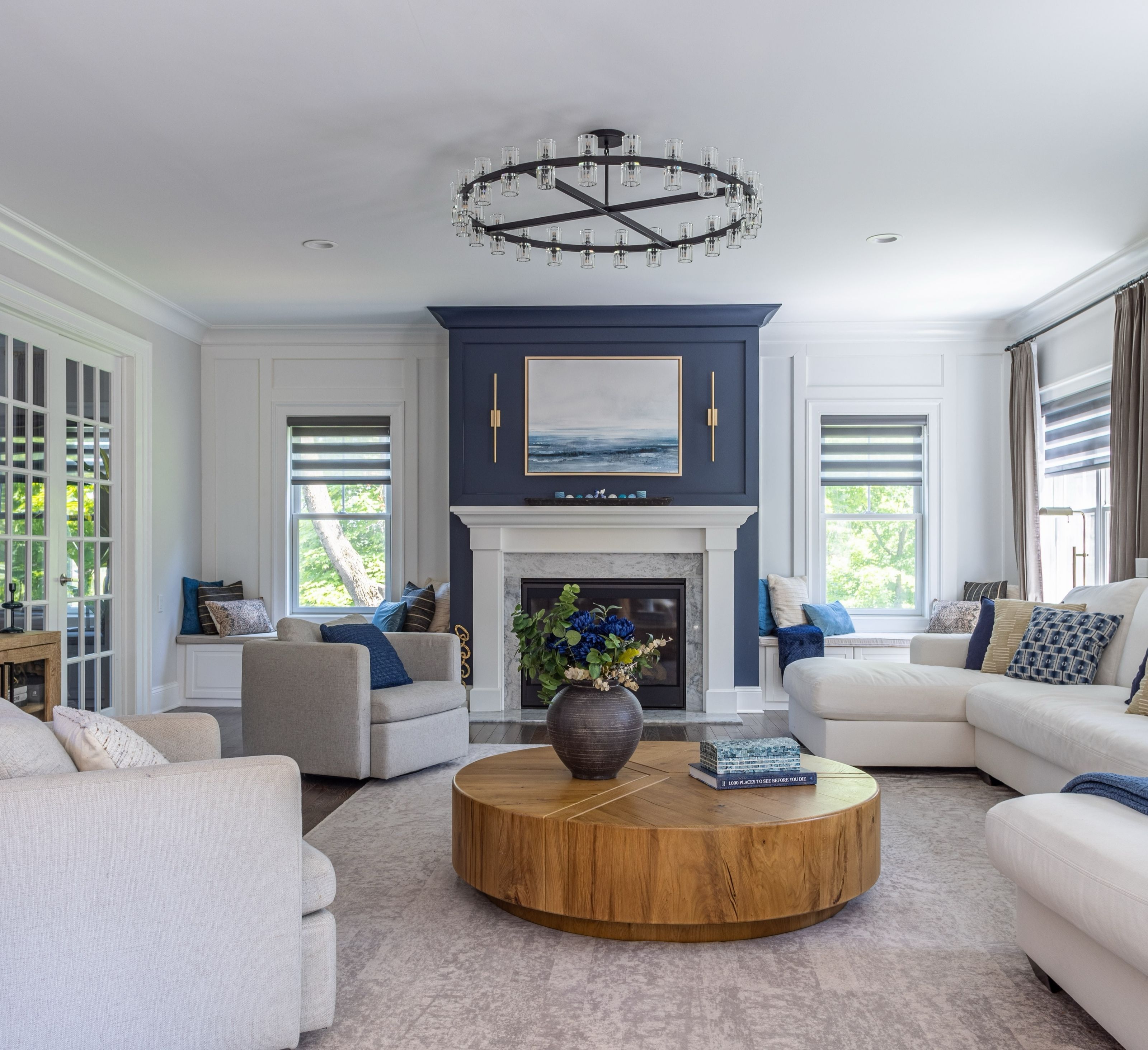 Living room with a navy panelled fireplace wall, a round wood coffee table, cream sofas and armchairs, and a gallery wall of framed prints.