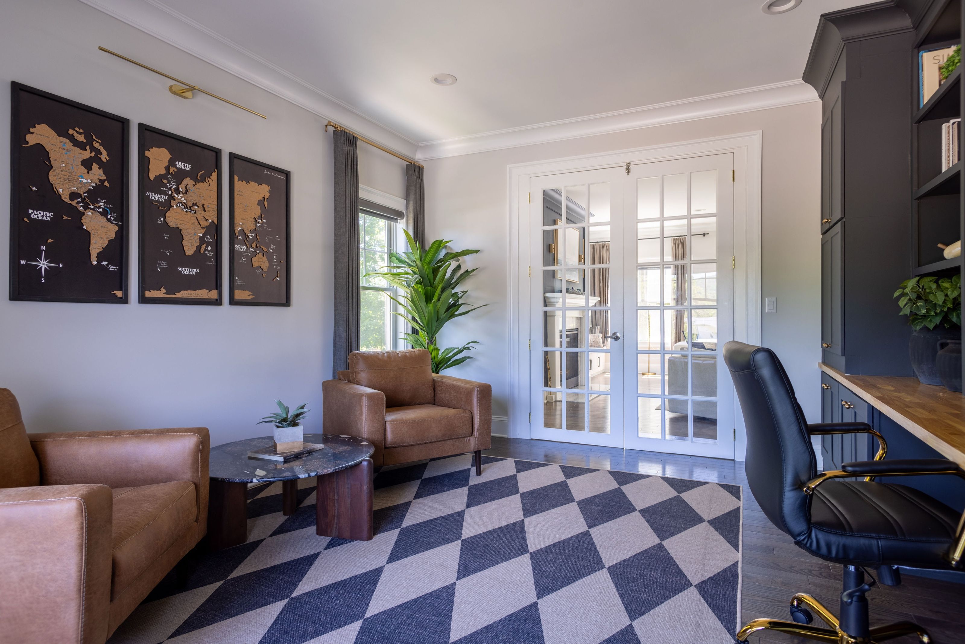 Home office with leather armchairs, a statement black marble and acacia wood coffee table, framed world maps, and French doors.