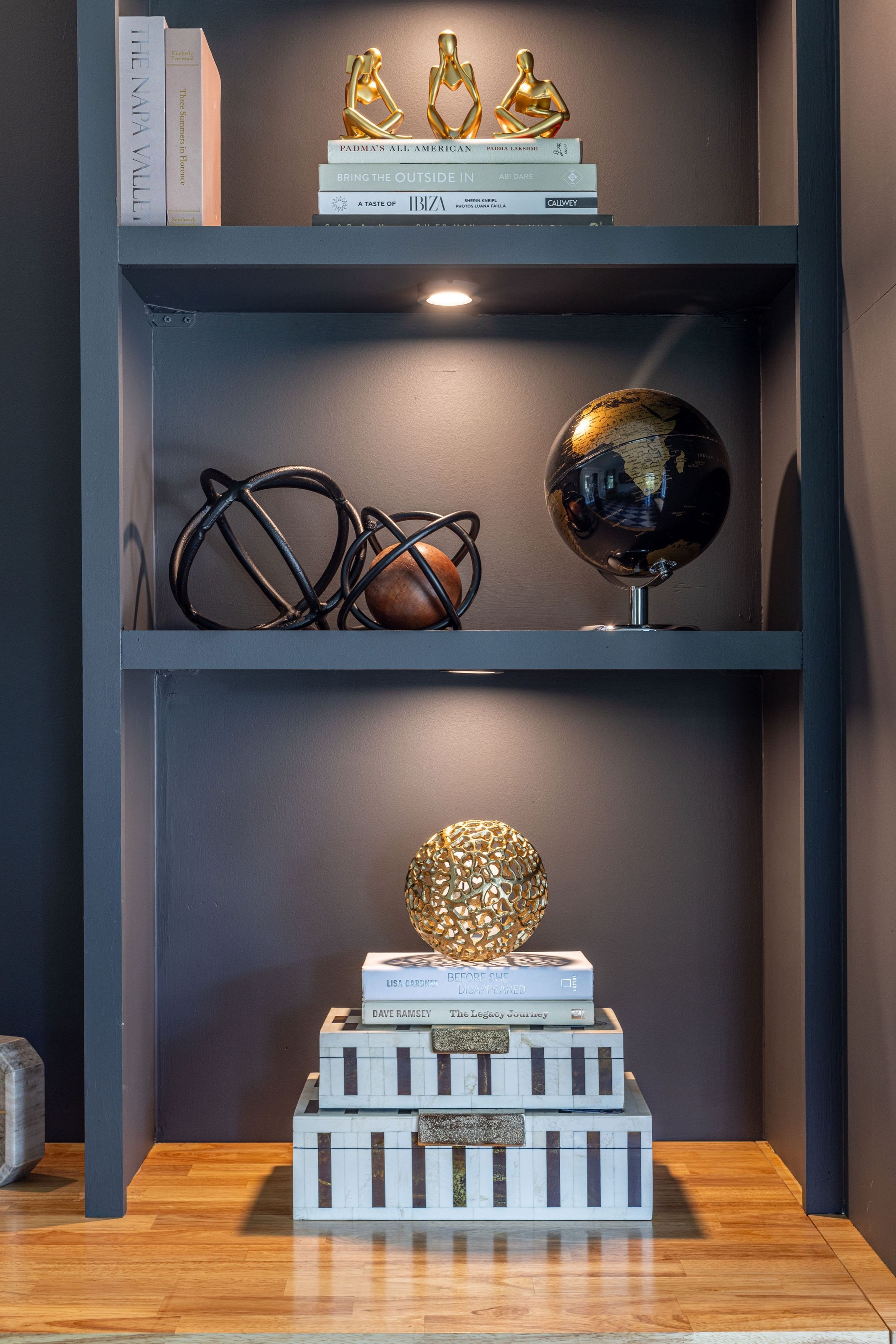 Custom office shelving styled with stacked books, dark iron spheres, a globe and a sculptural knot.