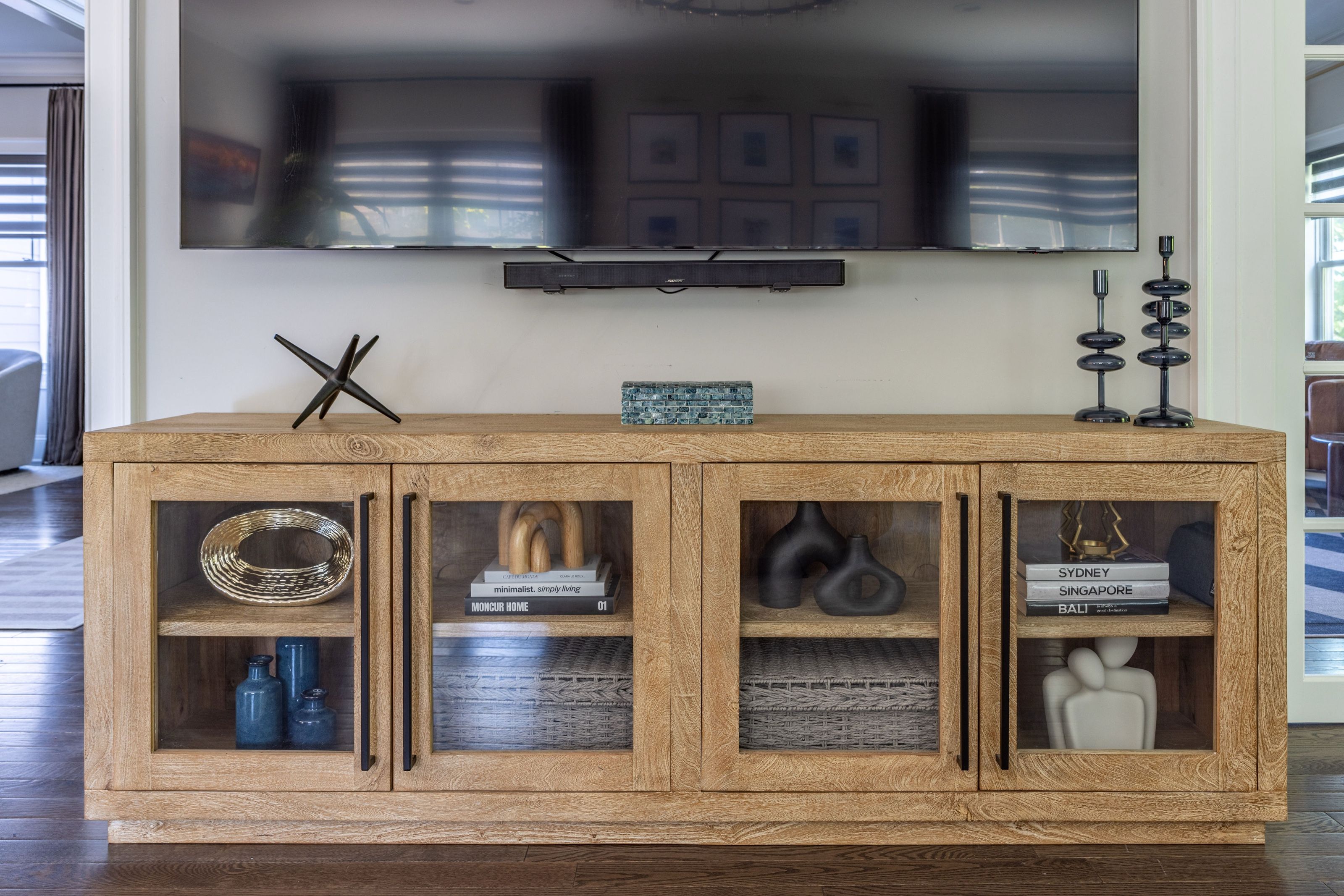 Oak media console with glass doors, styled with books, woven baskets, and sculptural objects.