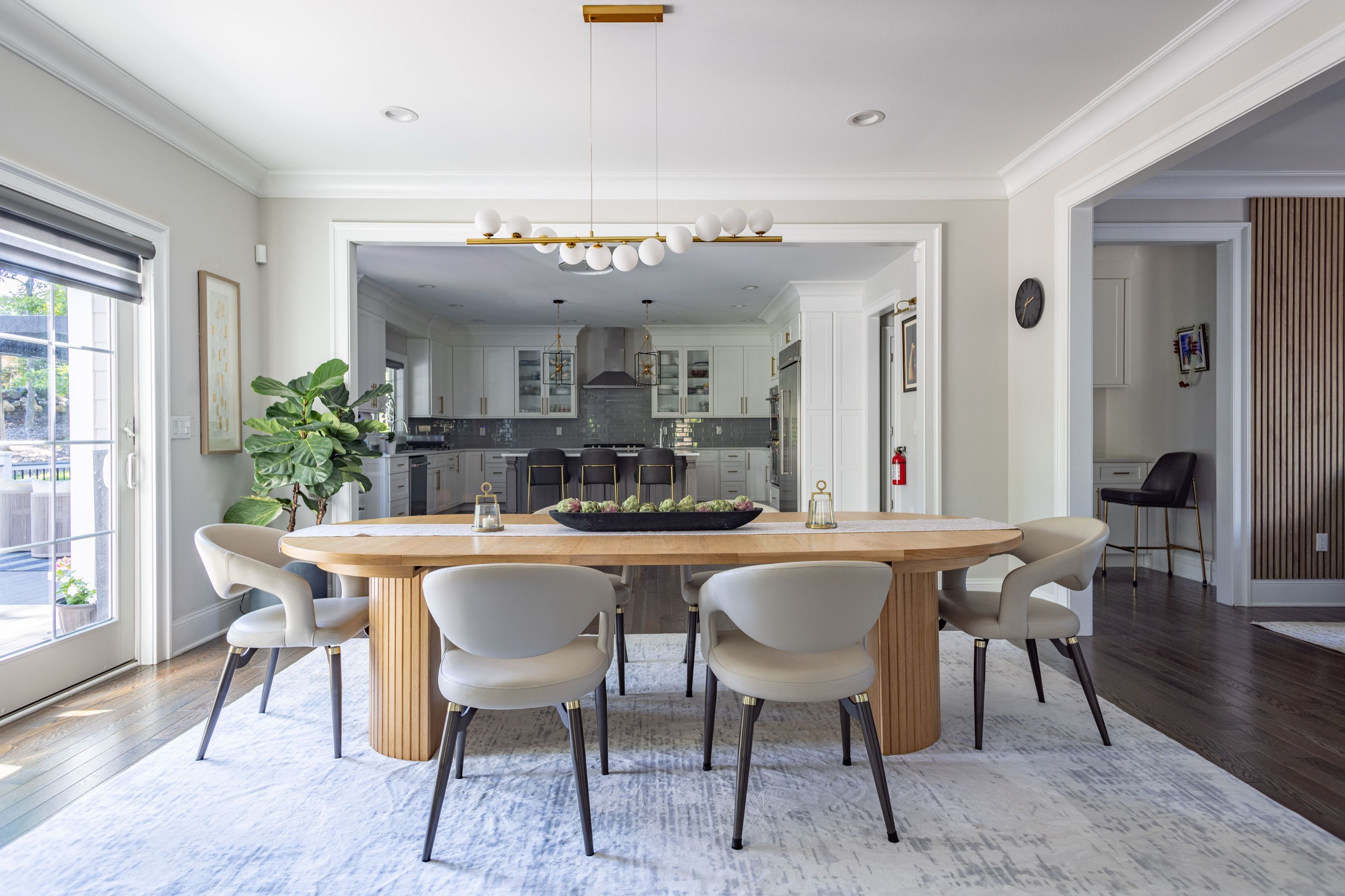Dining room with an oval wood table featuring fluted legs and upholstered chairs, viewed toward the adjoining kitchen.