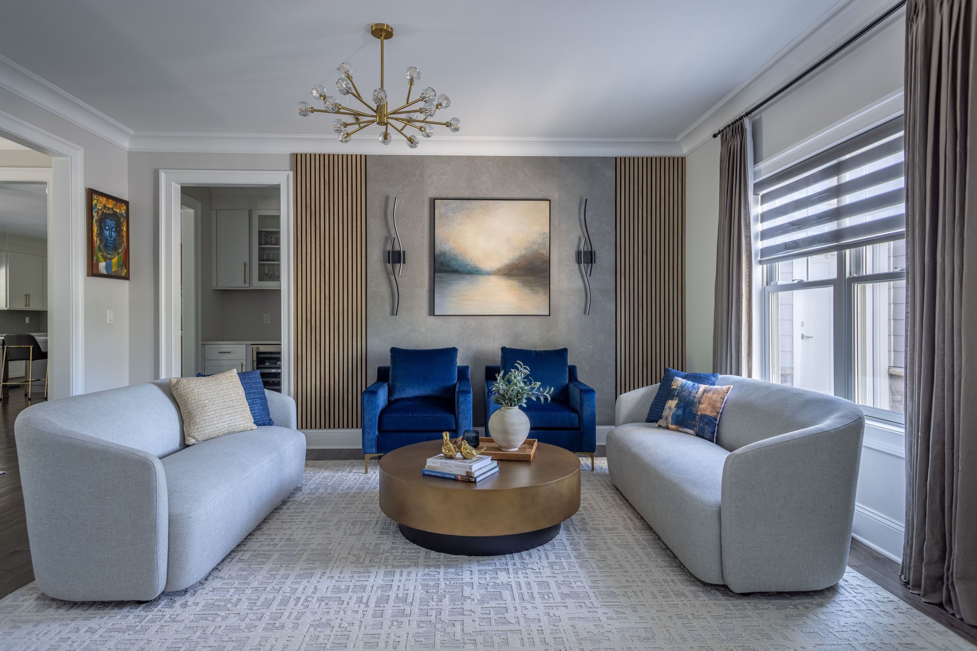 Transitional sitting room with pale sofas, royal blue velvet chairs, and a round brass coffee table.
