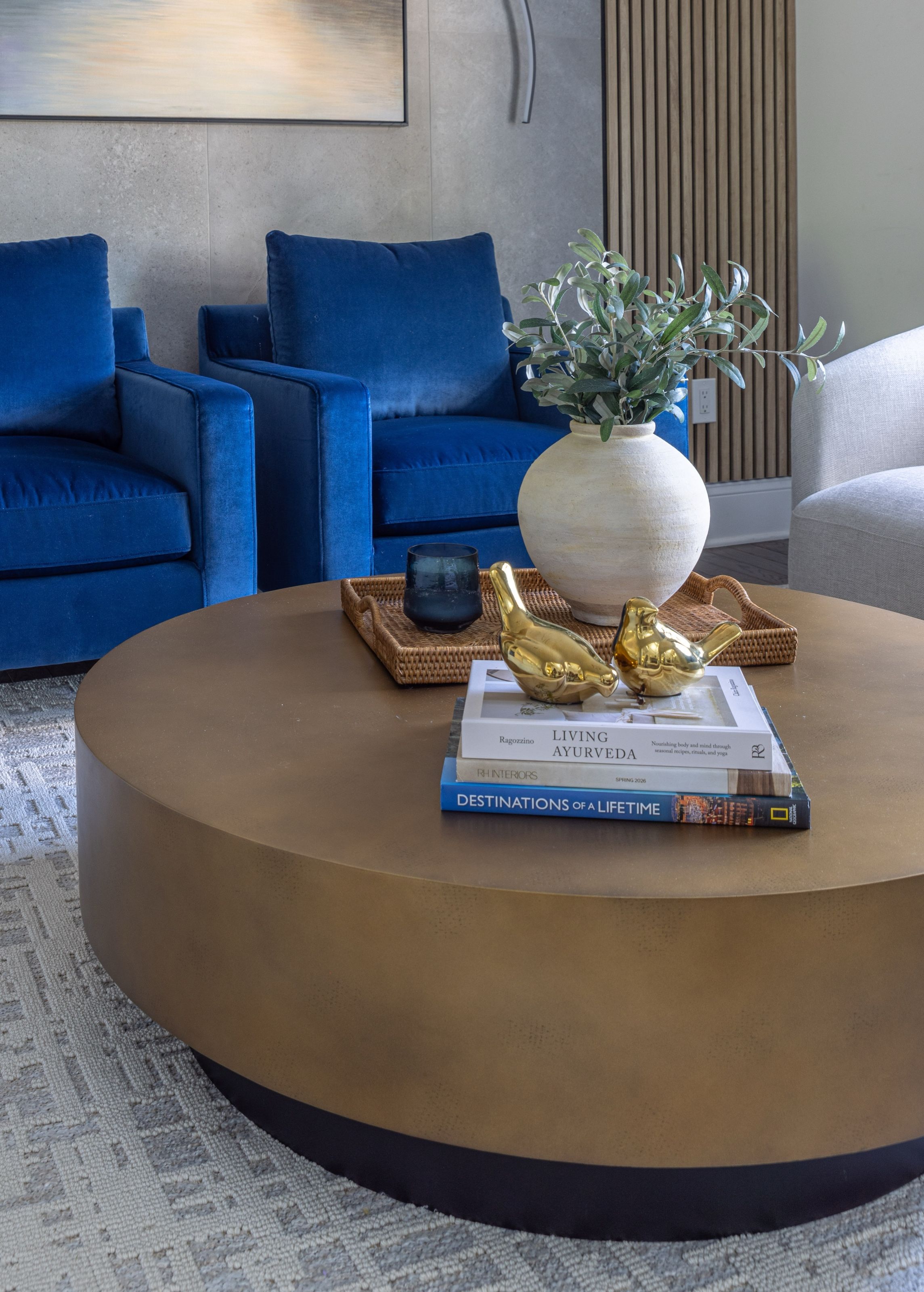 Brass coffee table styled with a woven tray, decorative brass birds, books, and olive branches.