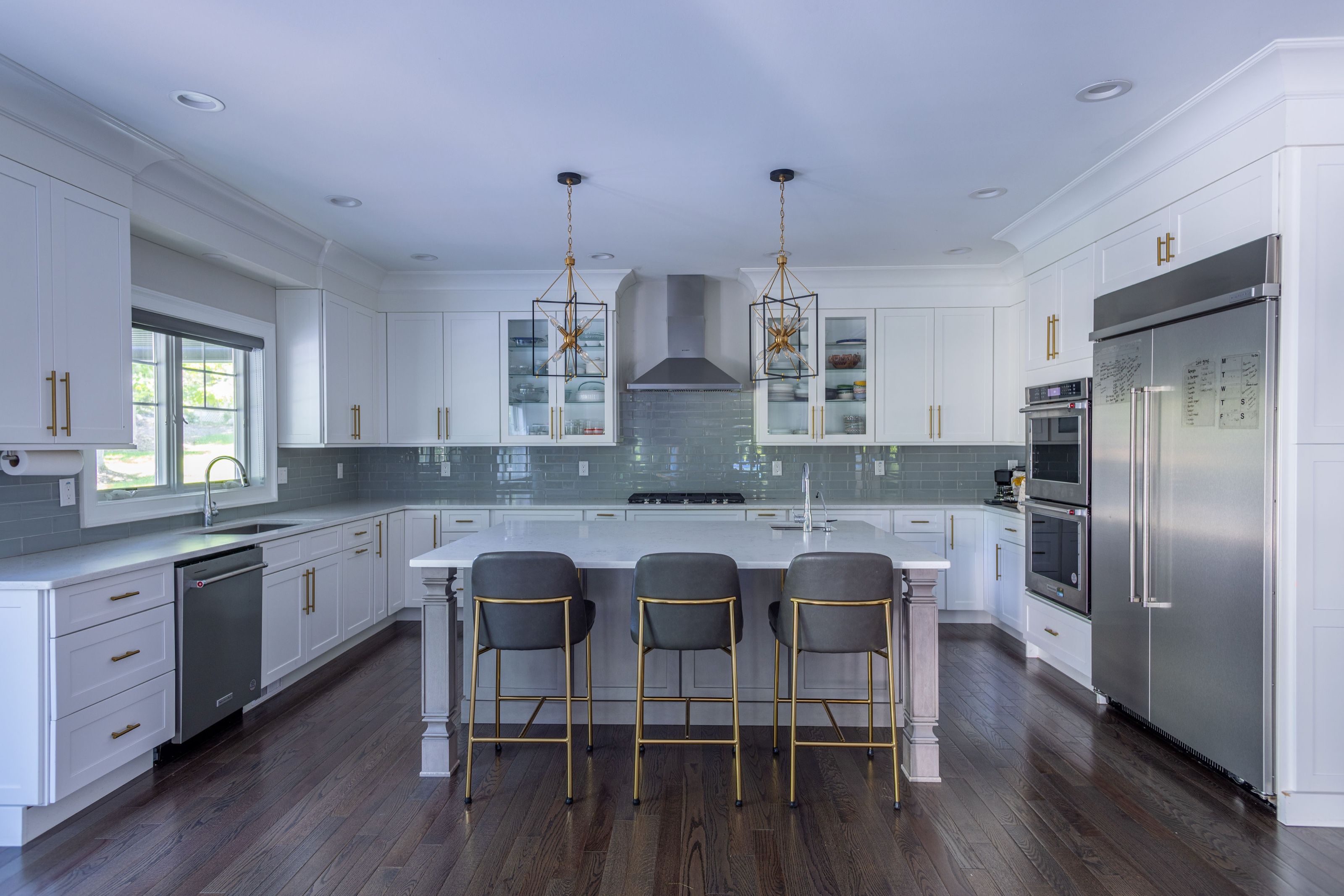 Transitional kitchen with white cabinetry, a glass-tile backsplash, gray island lantern pendants, and counter stools at the island.