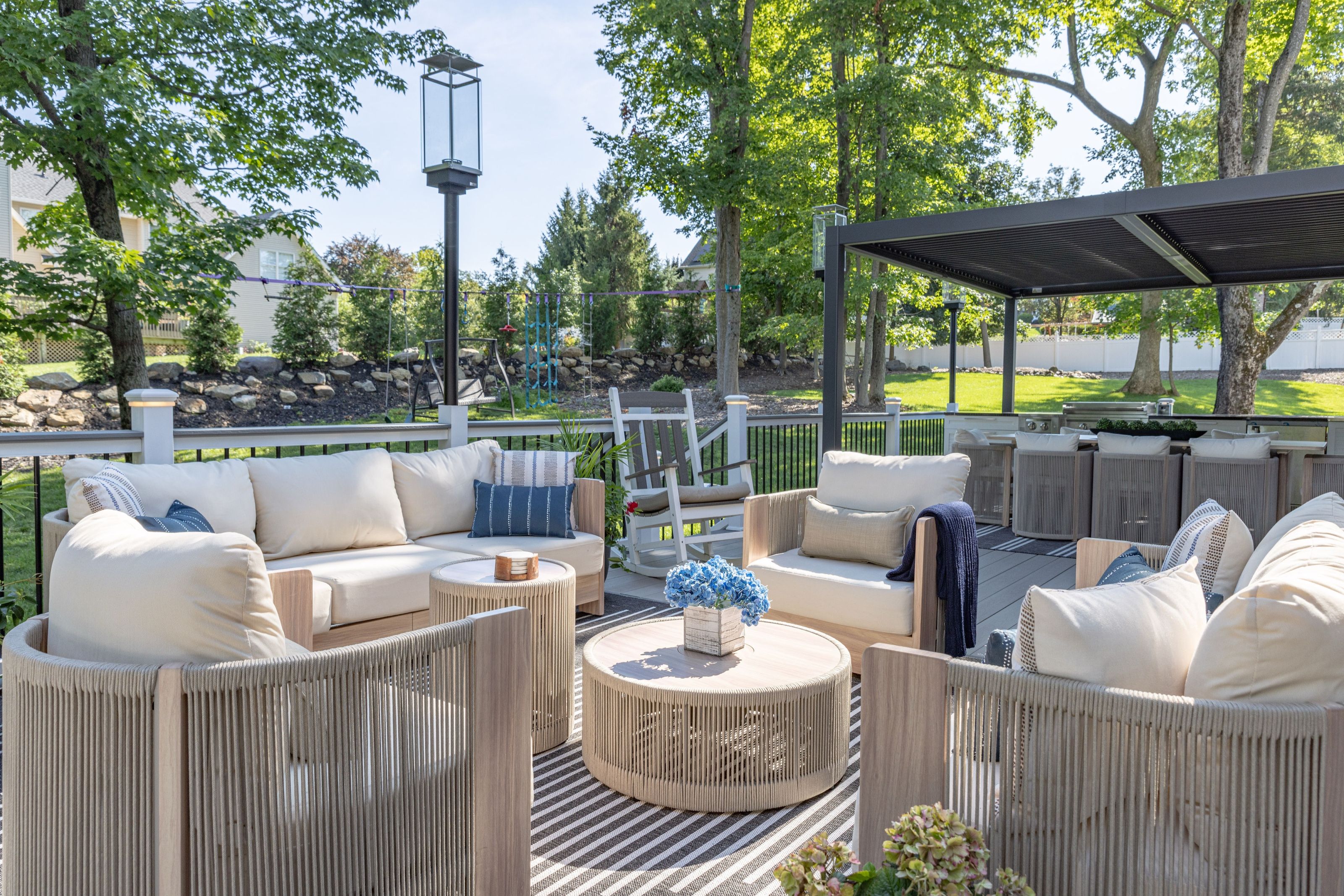 Outdoor entertaining area nestled among trees and lanterns, with woven lounge seating and a covered seating area beyond.