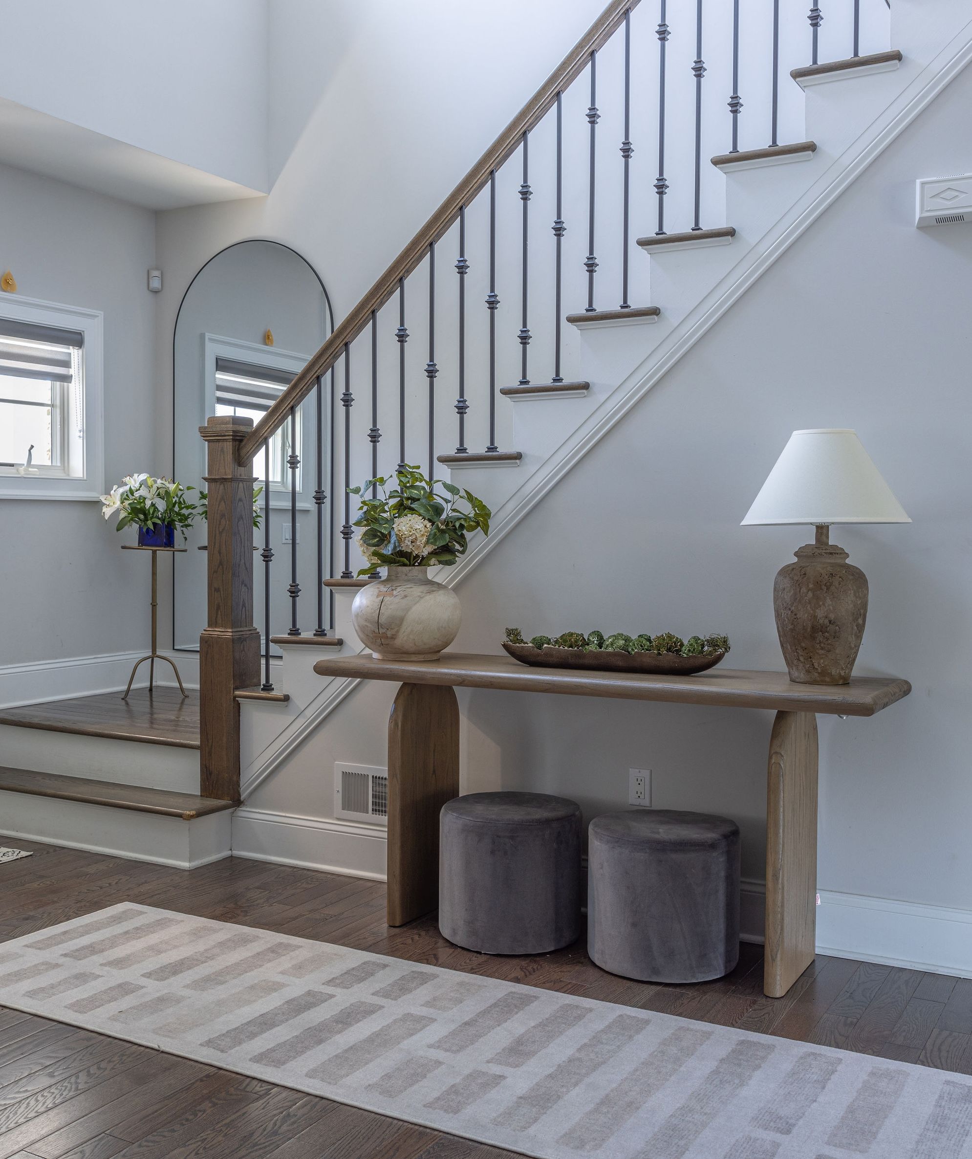 Warm foyer with a wood console table beneath the stairs, an arched mirror and stools underneath.