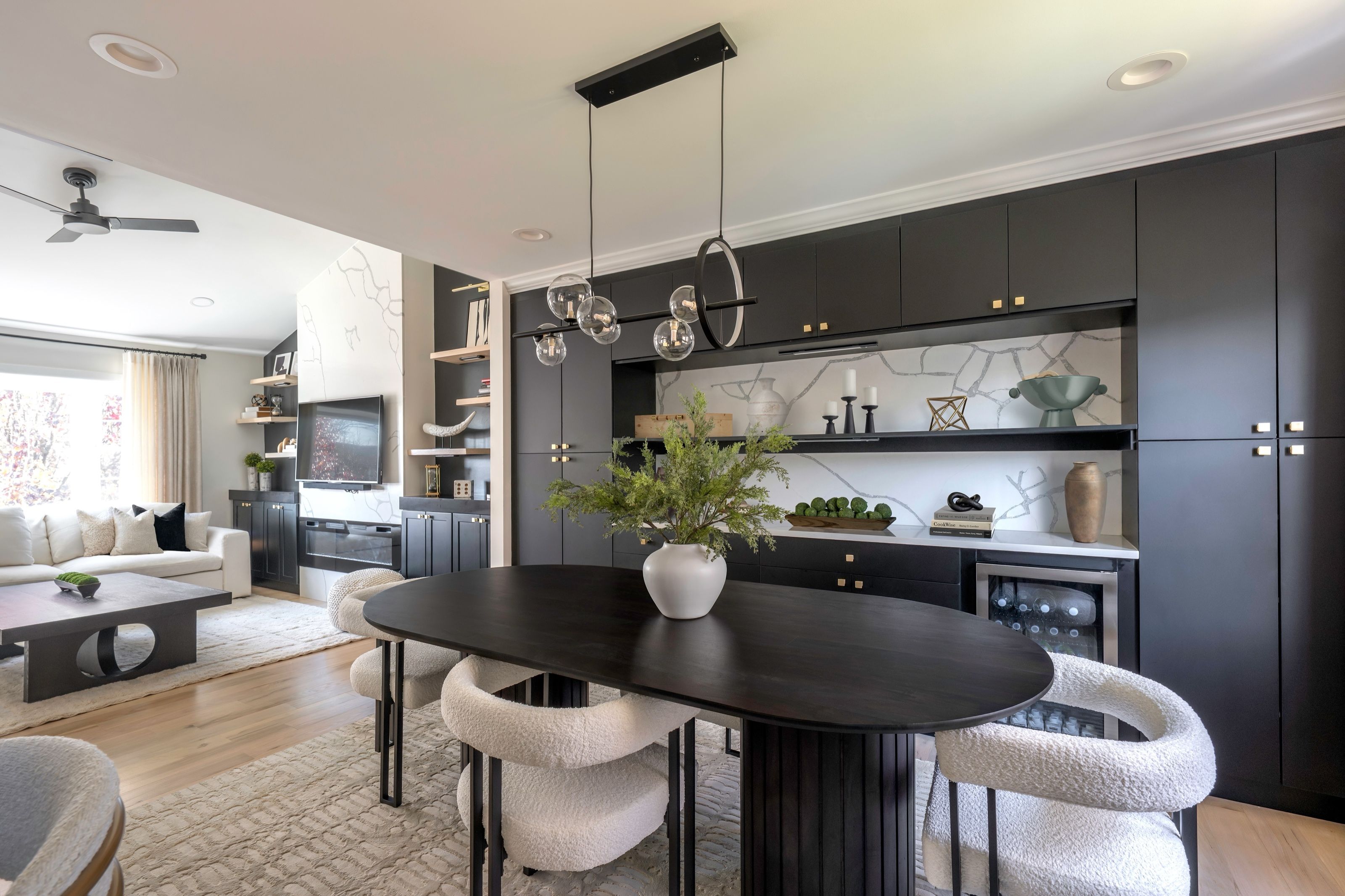 Dining area with an oval wood table against a wall of custom black cabinetry, opening to the adjoining living room.