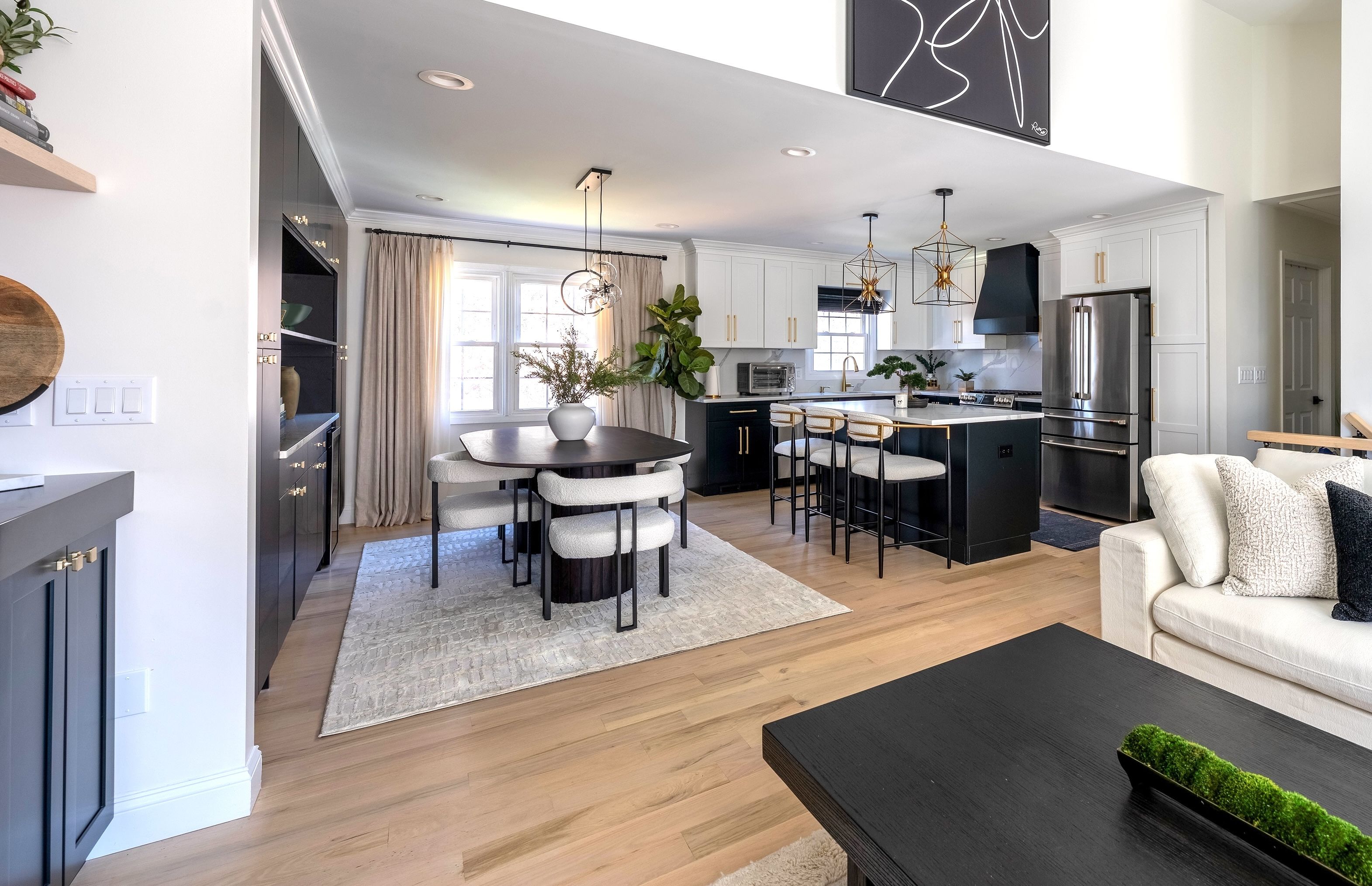 Renovated kitchen and dining area with white upper cabinetry, black lower cabinetry, brass pendant lights, and pale oak floors in a Monmouth County, New Jersey home.