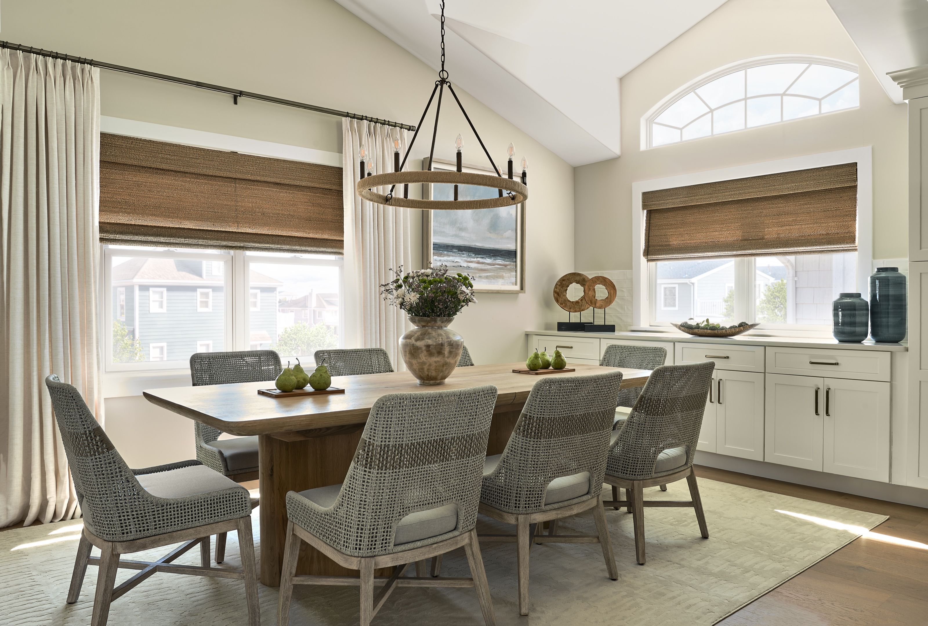 Coastal dining room with a round wood chandelier, long dining table, rope dining chairs, and arched window in a Jersey Shore home.