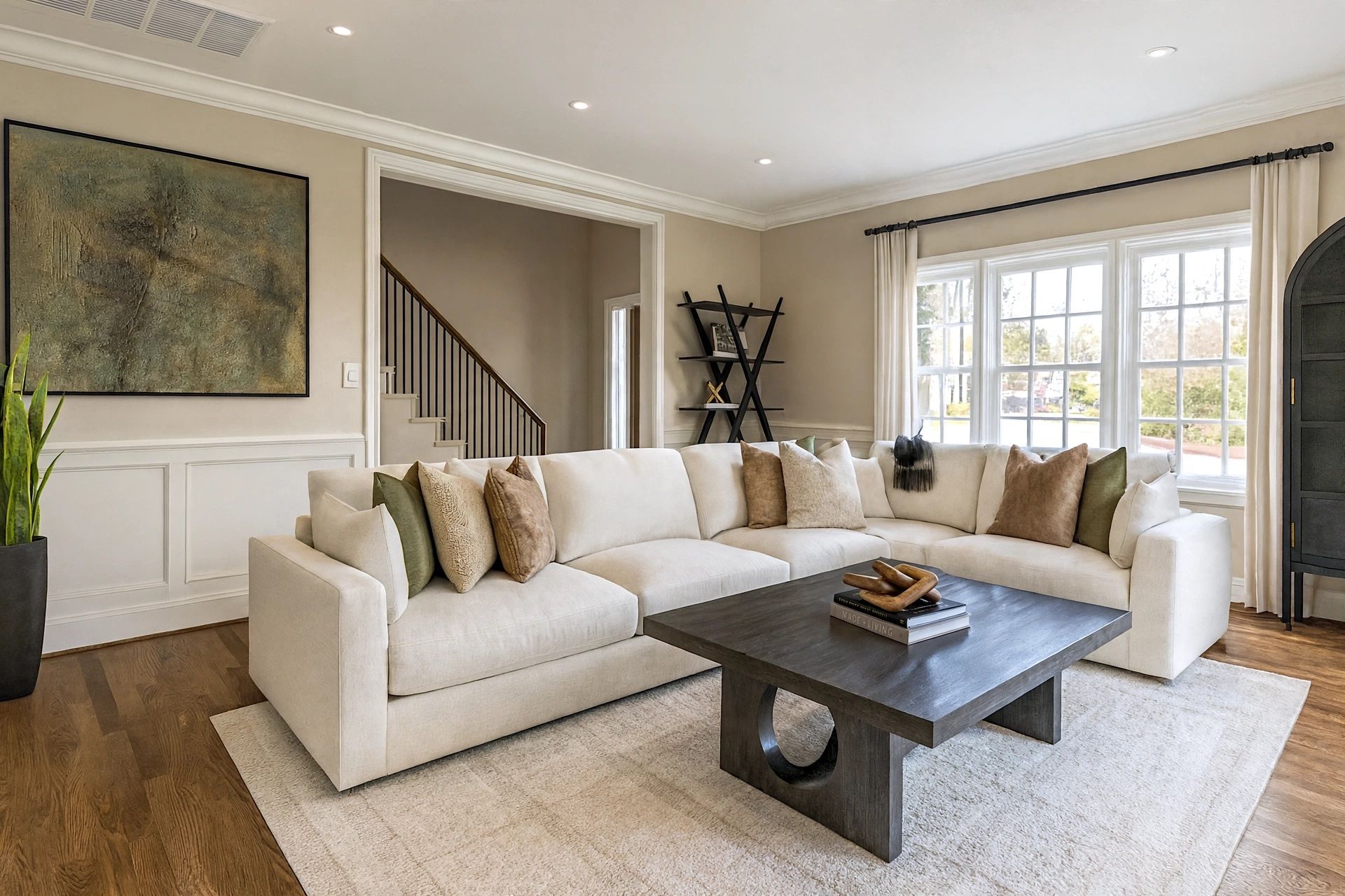 Living room with a large cream sectional arranged around a low dark coffee table, abstract artwork, and a staircase with display shelving beyond.