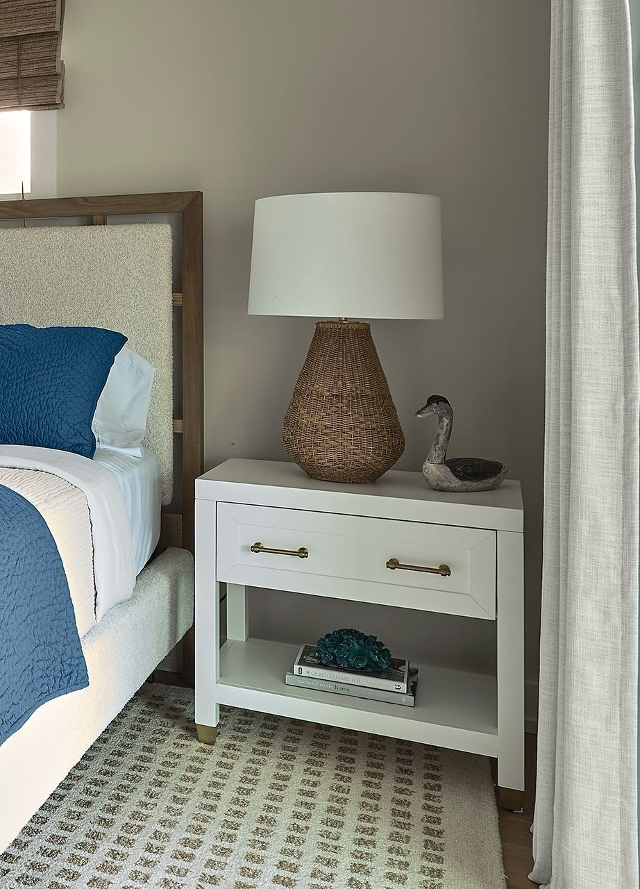 Bedside table with a woven lamp and carved bird sculpture.