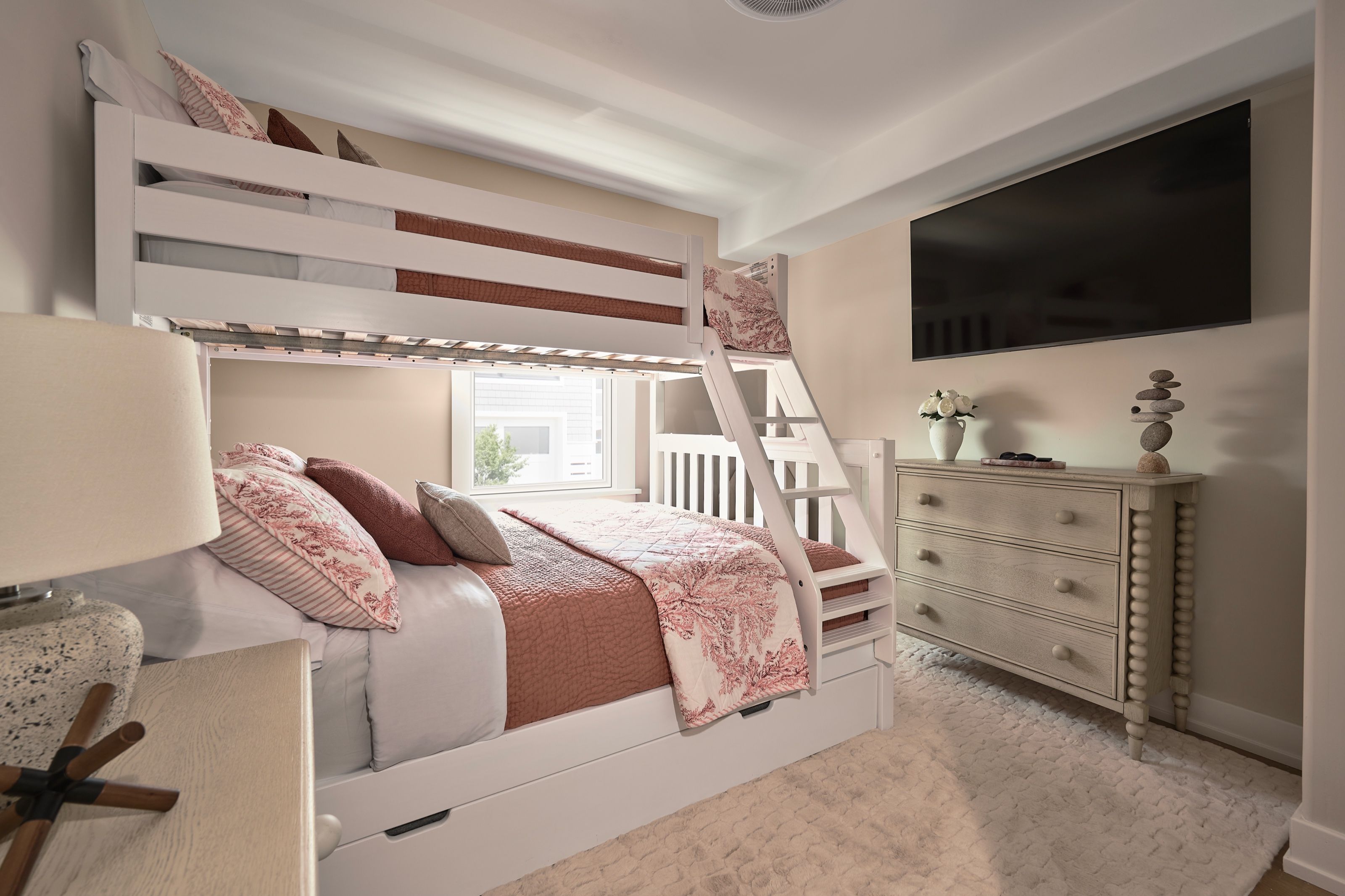 Coastal bunk room with coral accents, a twin-over-queen bunk bed, plush cream washable rug, and wall-mounted television.