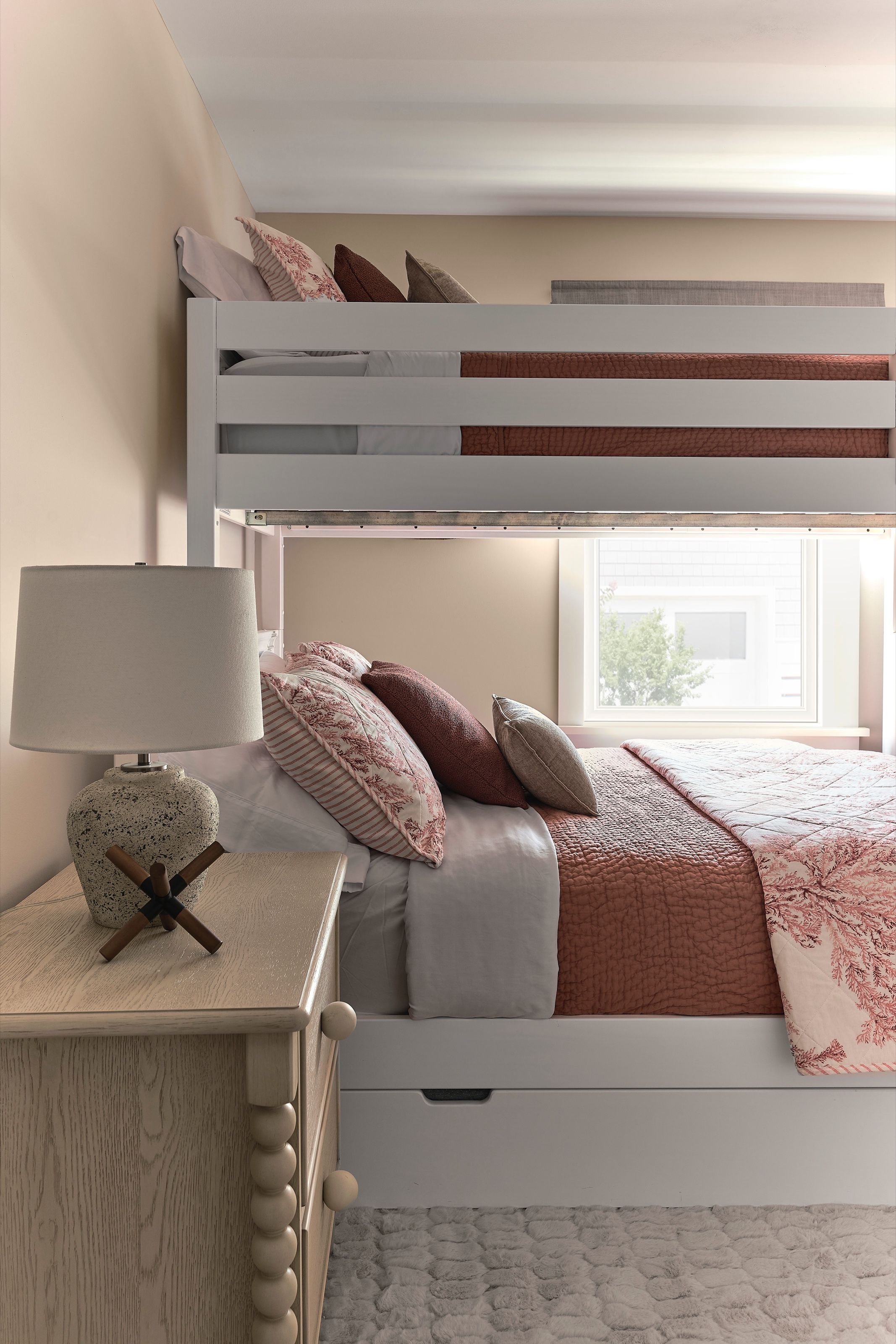 Side view of a bunk room with a dresser and table lamp beside the beds.