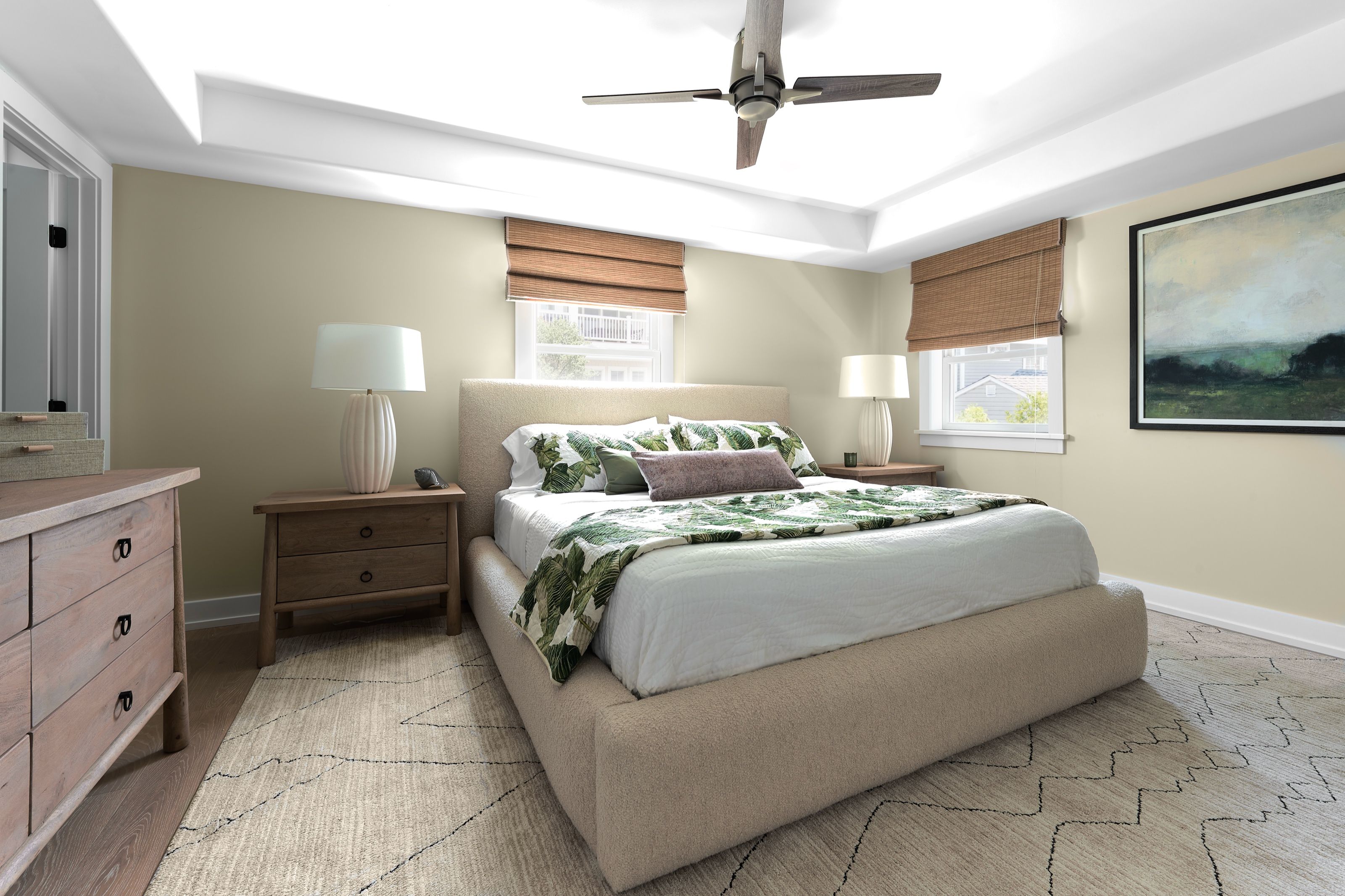 Coastal bedroom with an upholstered bed, palm-print bedding, and landscape artwork.