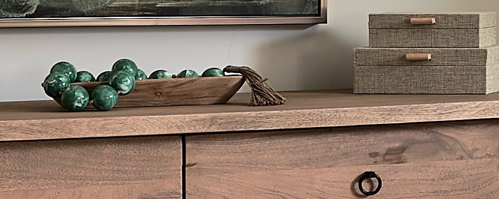Close-up of a bedroom dresser with a wooden bowl of green glass beads and two woven boxes.