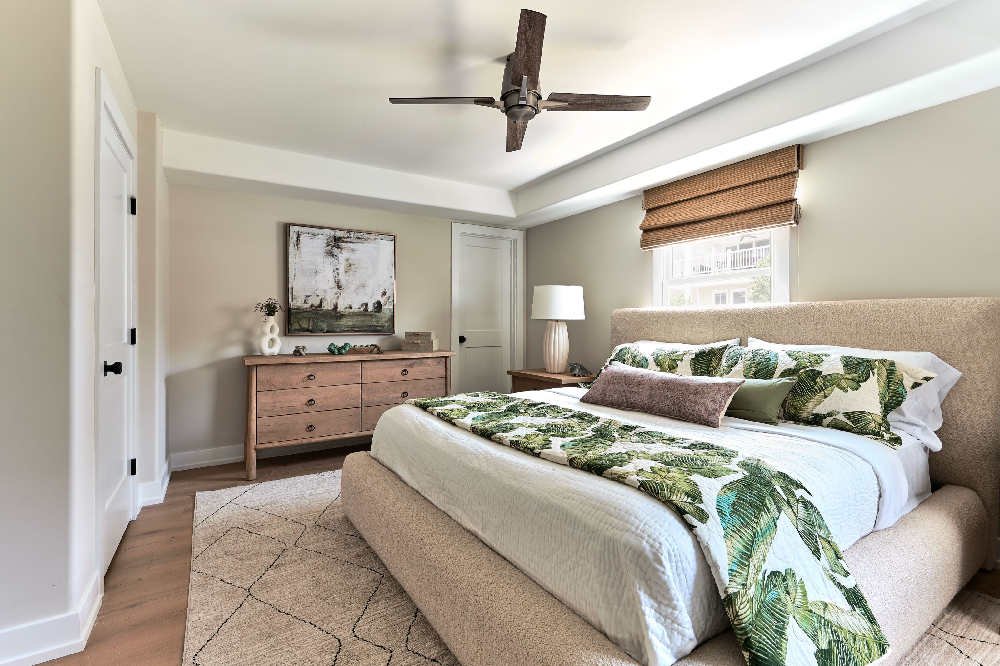 Guest bedroom viewed from the doorway, showing an upholstered bed and wood dresser beneath abstract artwork.
