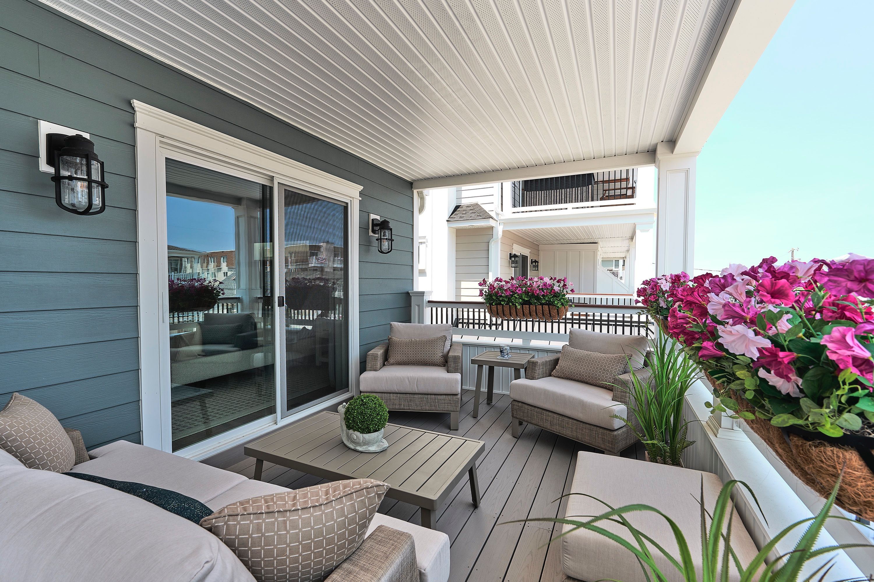 Furnished bedroom balcony with wicker seating and flowering railing planters.