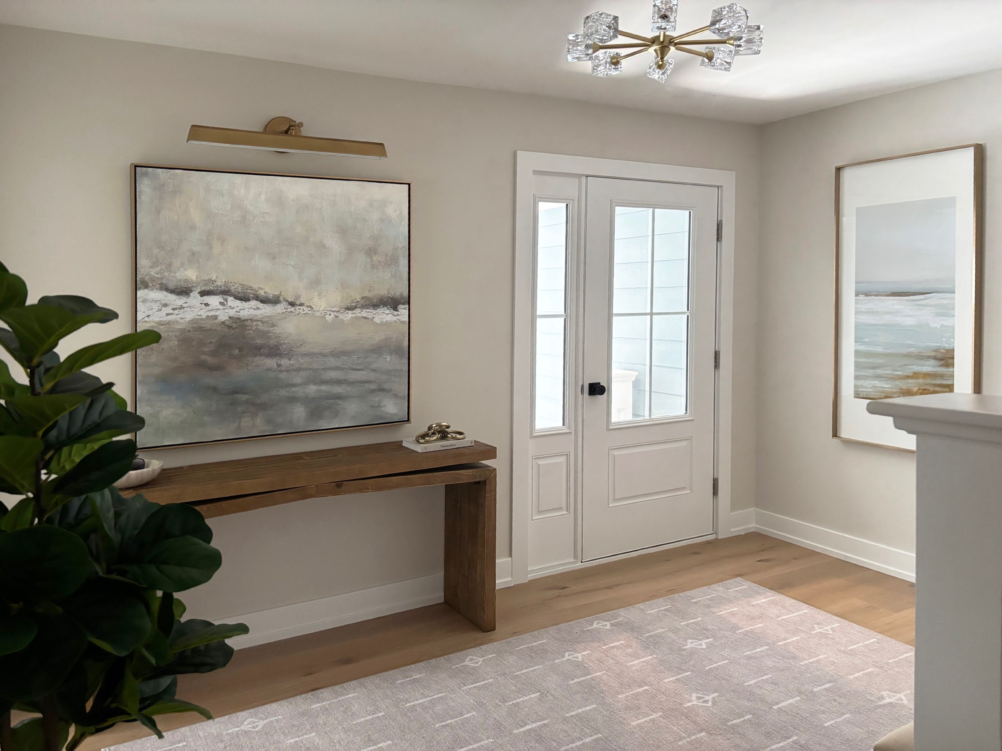 Entryway with a worn oak wood console beneath a large abstract seascape and a glass front door.