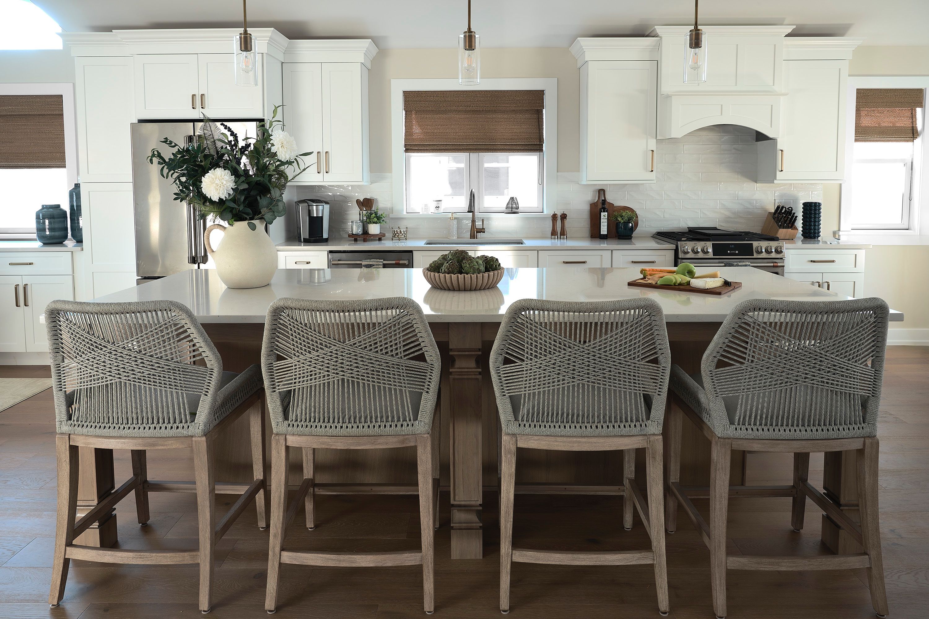 Front view of a kitchen island with four woven counter stools and pendant lights above.