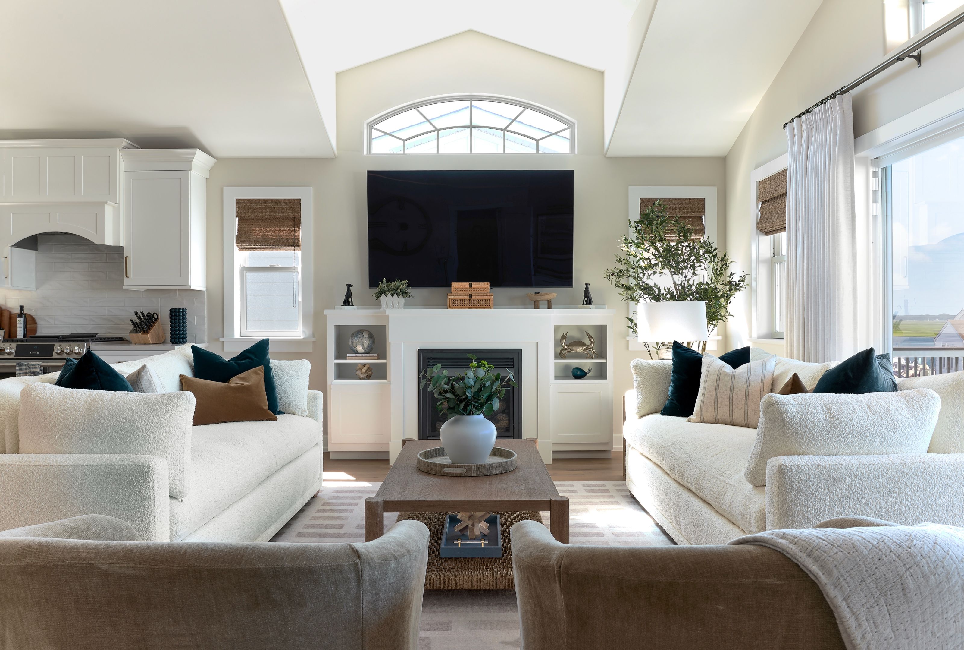 Living room with white sofas facing a fireplace and television, flanked by built-in cabinetry and an arched window.