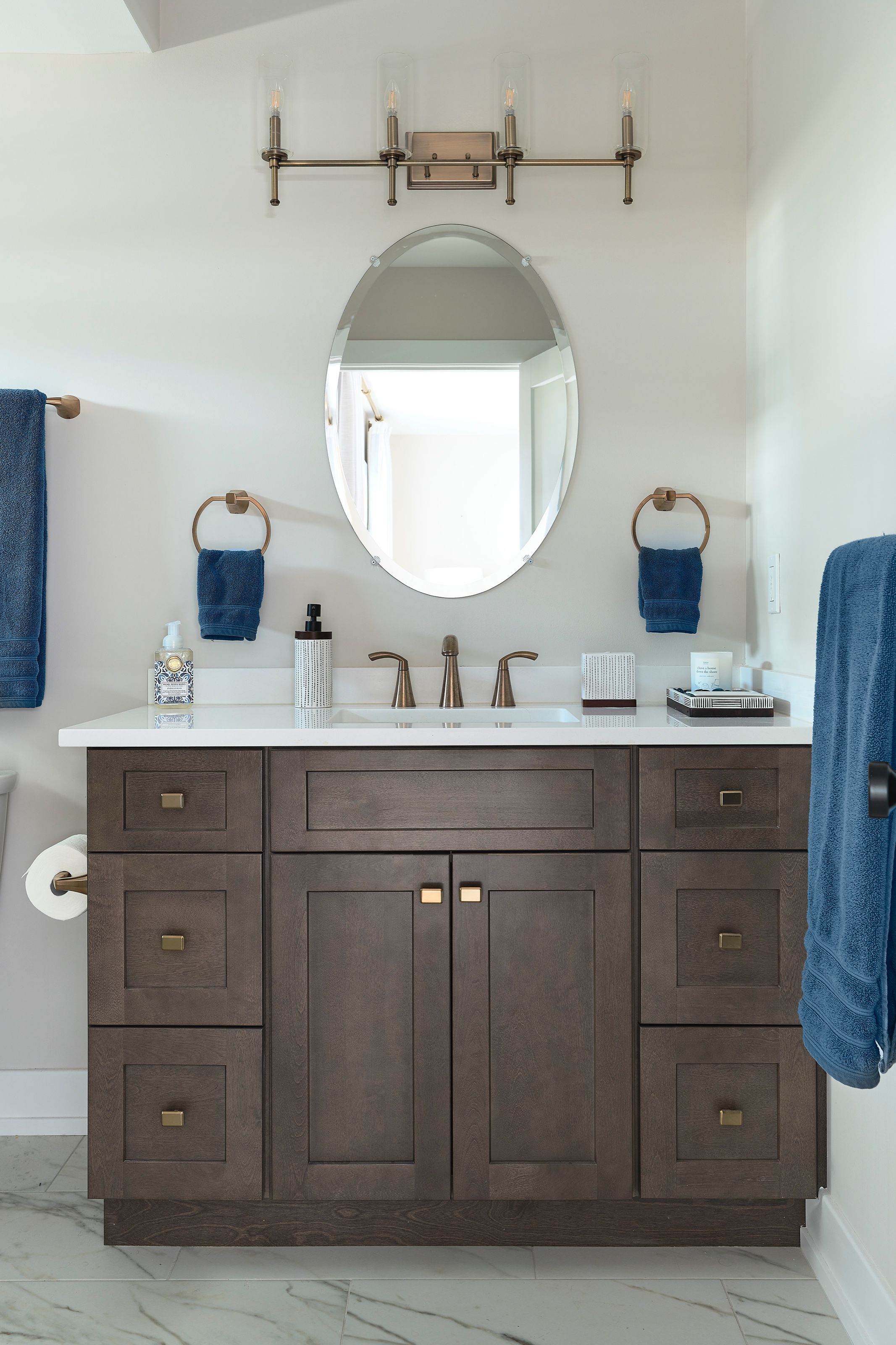 Bathroom with a dark wood vanity, oval mirror, and wall sconces.
