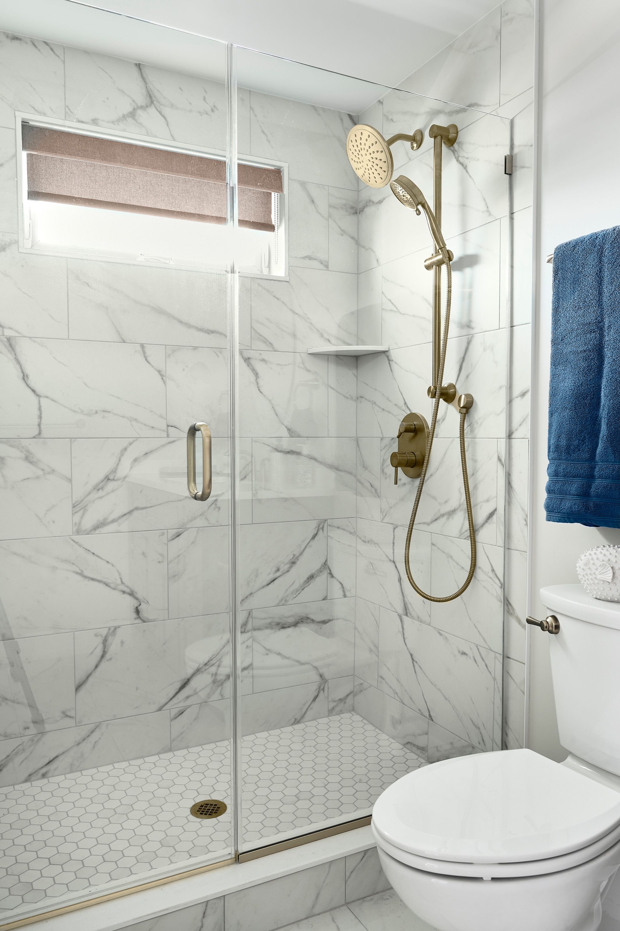 Bathroom shower with marble tile and brass fixtures.