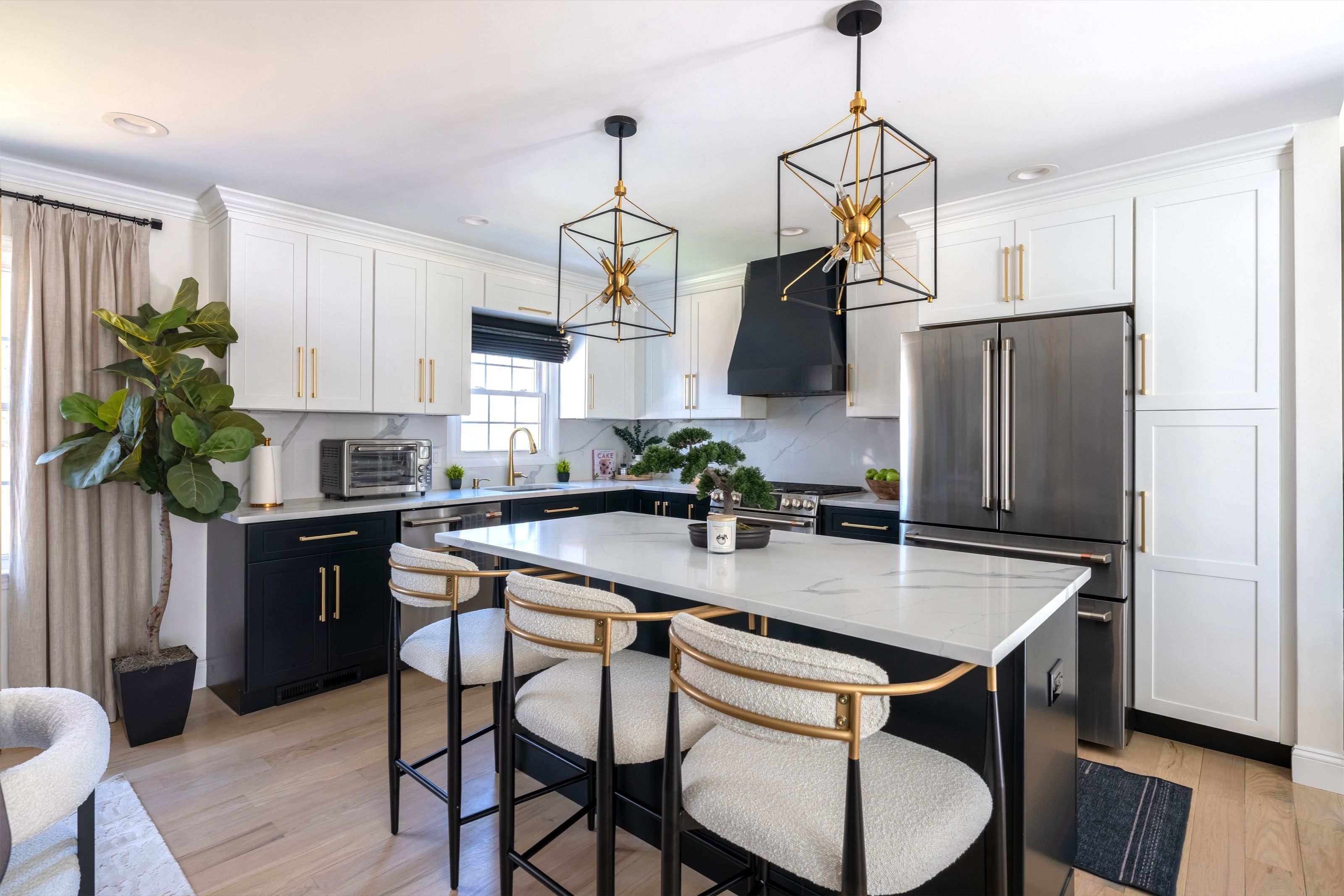 Renovated kitchen with black lower cabinetry, a white quartz island, black range hood, and brass lantern pendants.