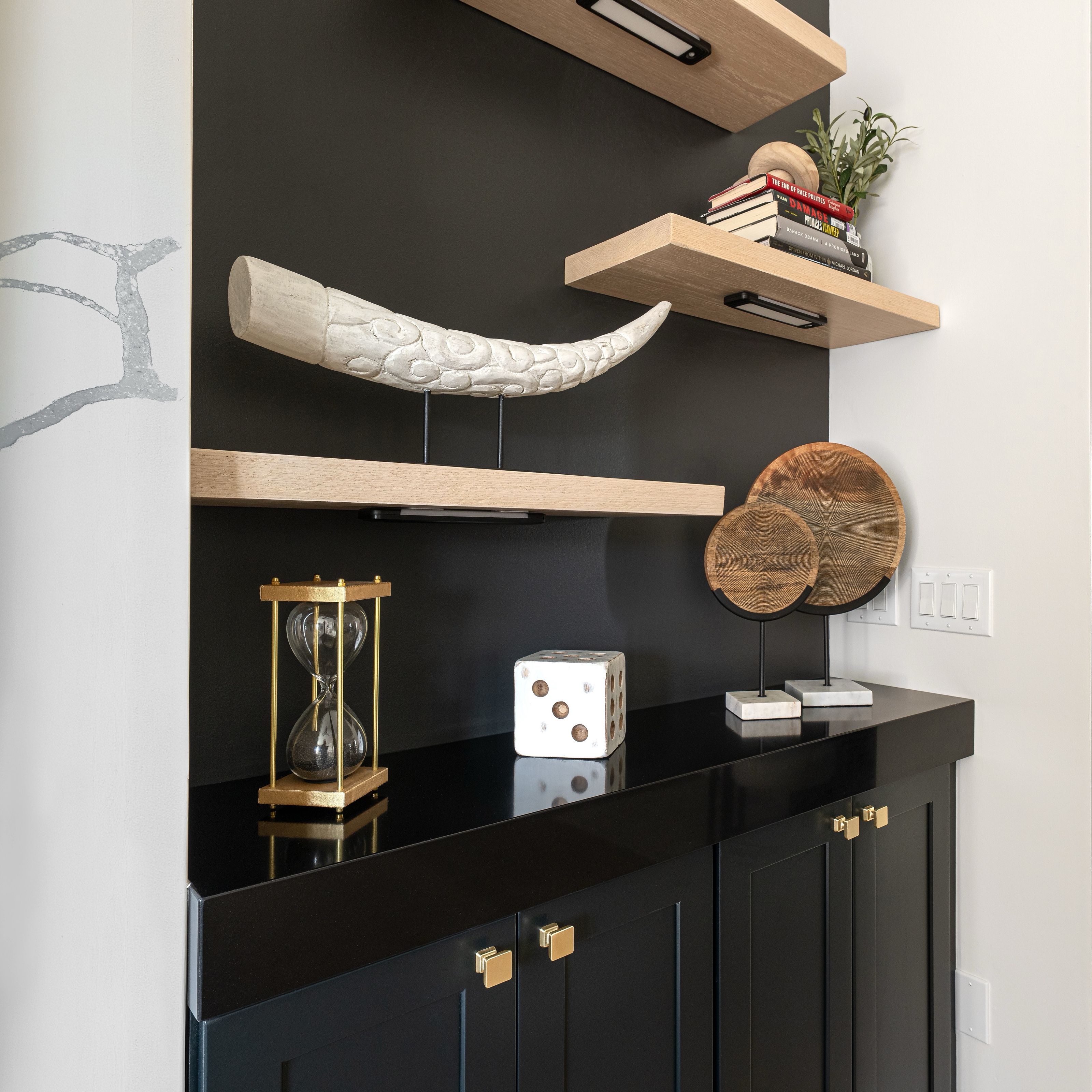 Custom oak floating shelves against black cabinetry, styled with carved sculptures, books and decorative objects.