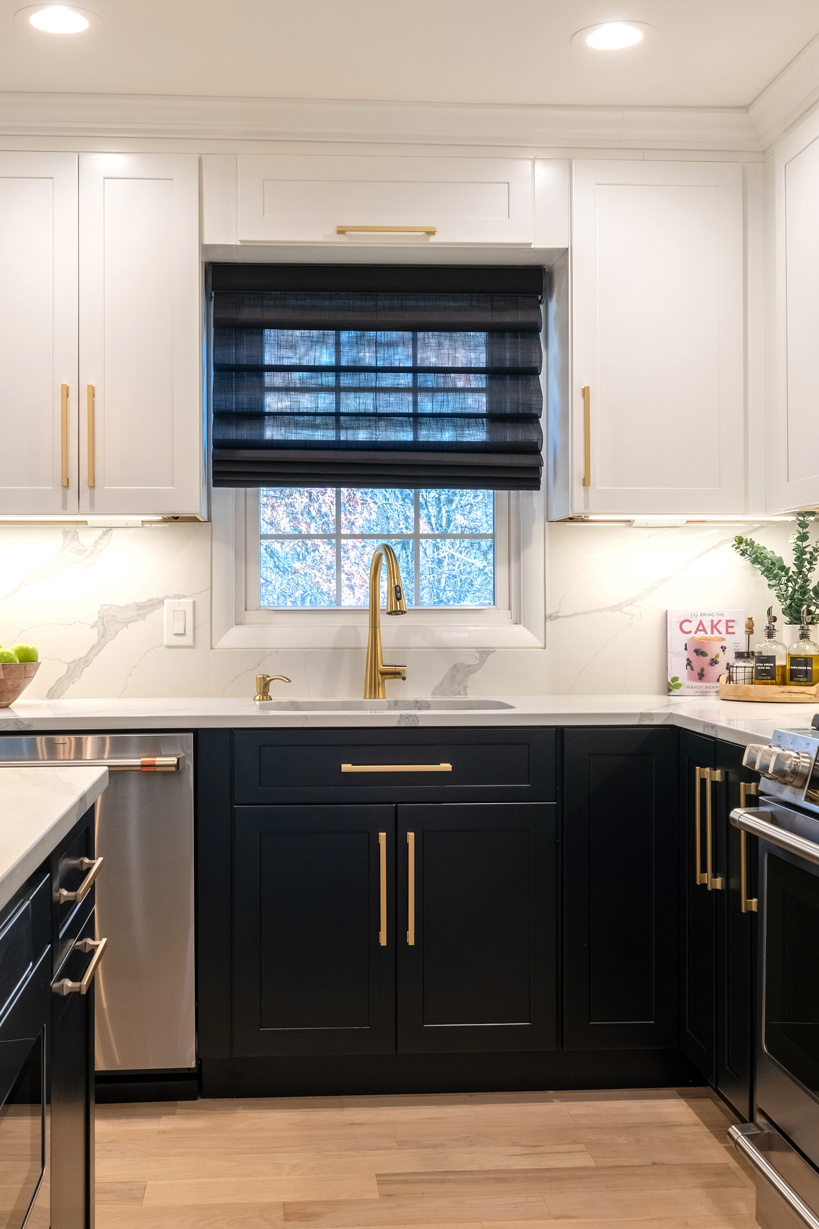 Kitchen sink beneath a window with a custom window treatment, featuring a brass faucet and marble backsplash.